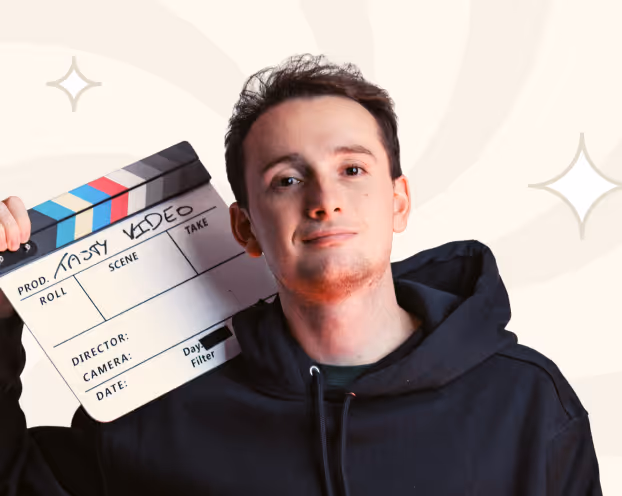 Jeune homme portant un sweat à capuche noir tenant une claque de cinéma avec l'inscription "Tasty Video".