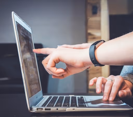 Deux mains interagissant avec un ordinateur portable ouvert, une main pointant vers l'écran et l'autre tapant sur le clavier.