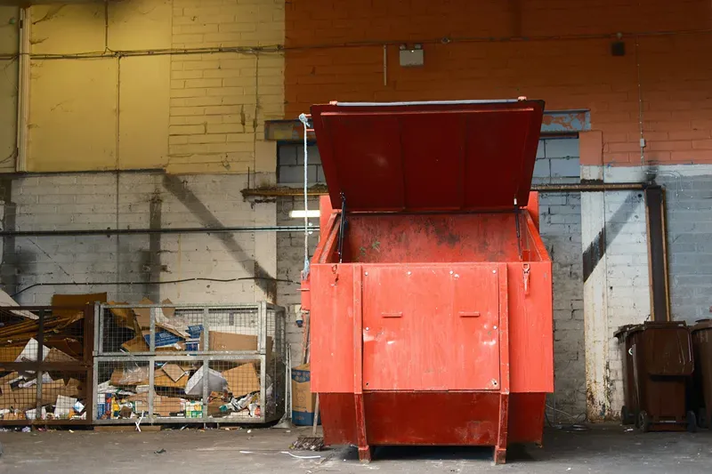 Compactor service for heavy-duty waste equipment, showing a large red industrial compactor with its loading lid open.
