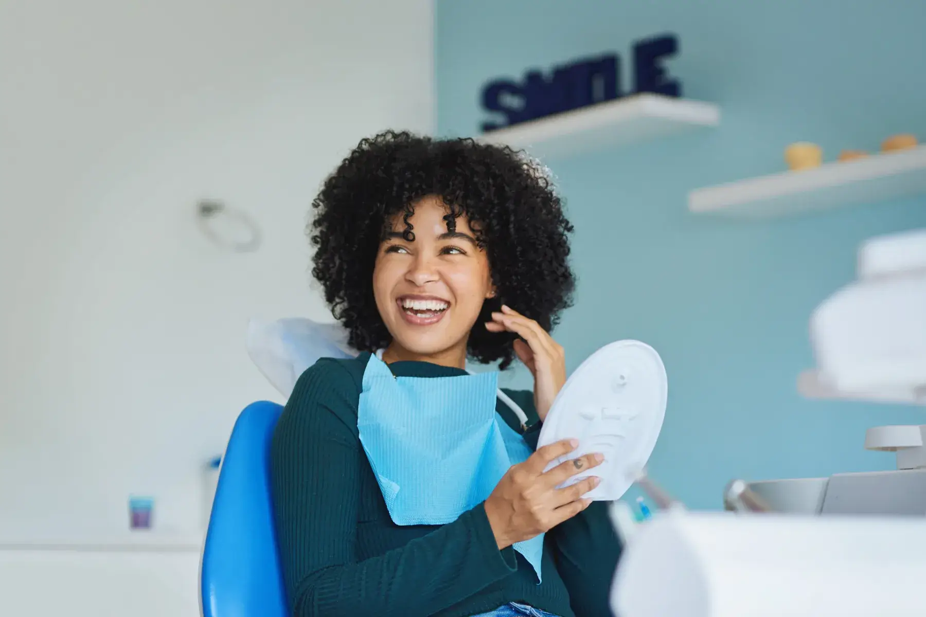 Smiling woman with curly hair sitting in a dental chair holding a white dental mold.