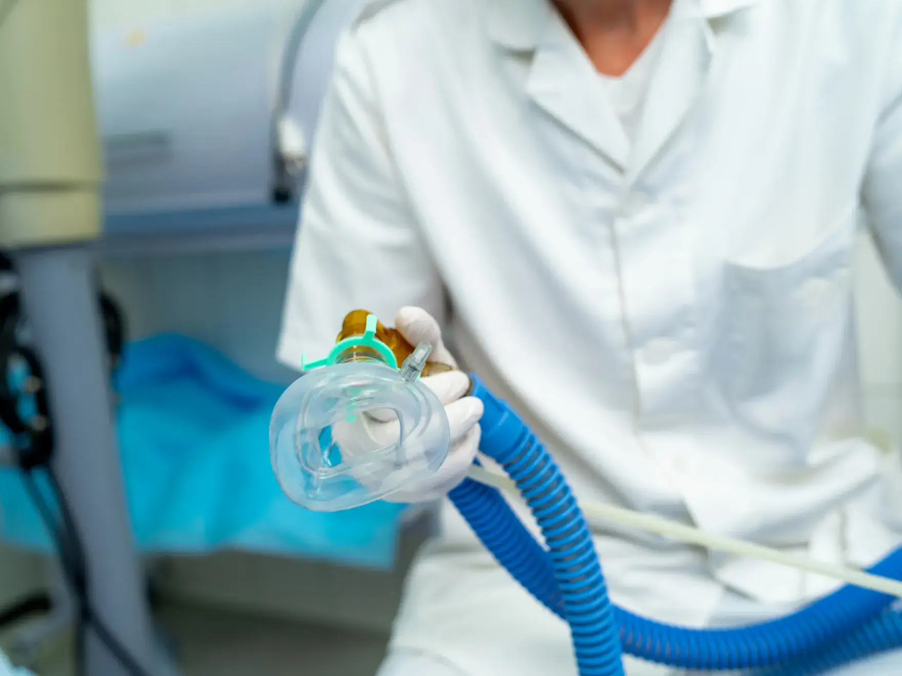 Healthcare professional in white uniform holding a clear oxygen mask connected to a blue corrugated hose.