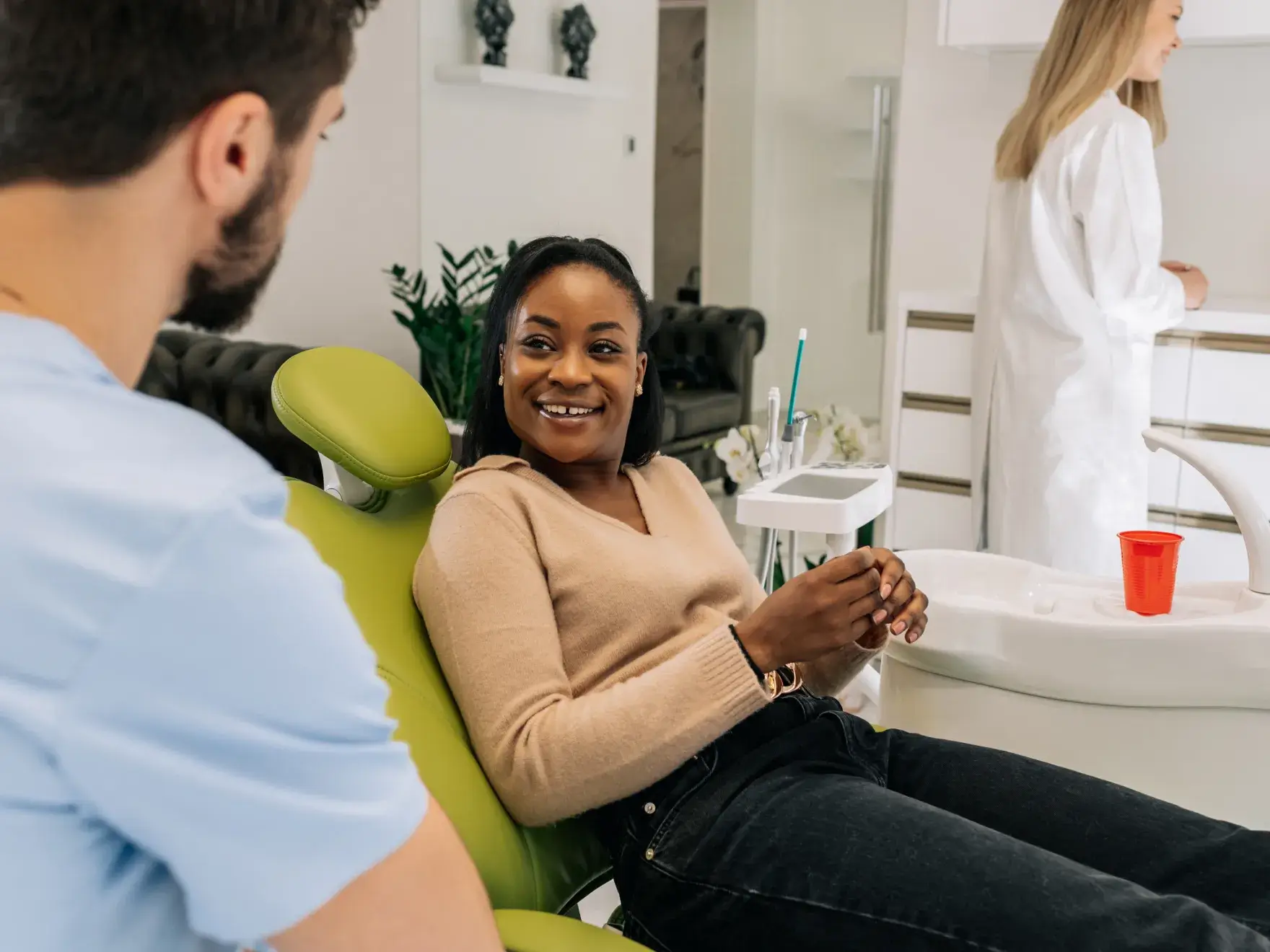 Smiling woman sitting in a green dental chair talking to a male dentist in a dental clinic.