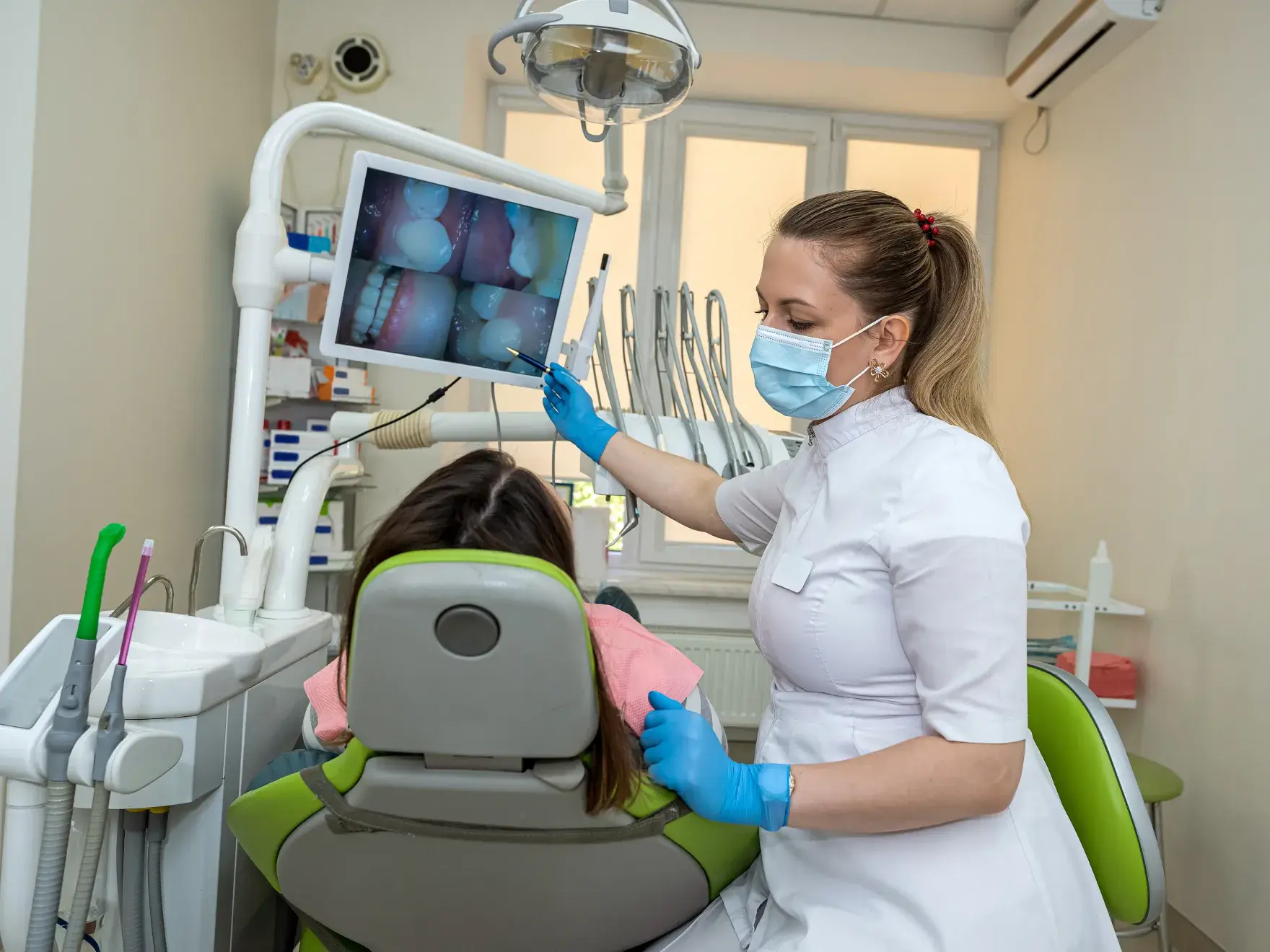Dentist wearing a mask and gloves showing dental x-ray images to a patient seated in a dental chair.