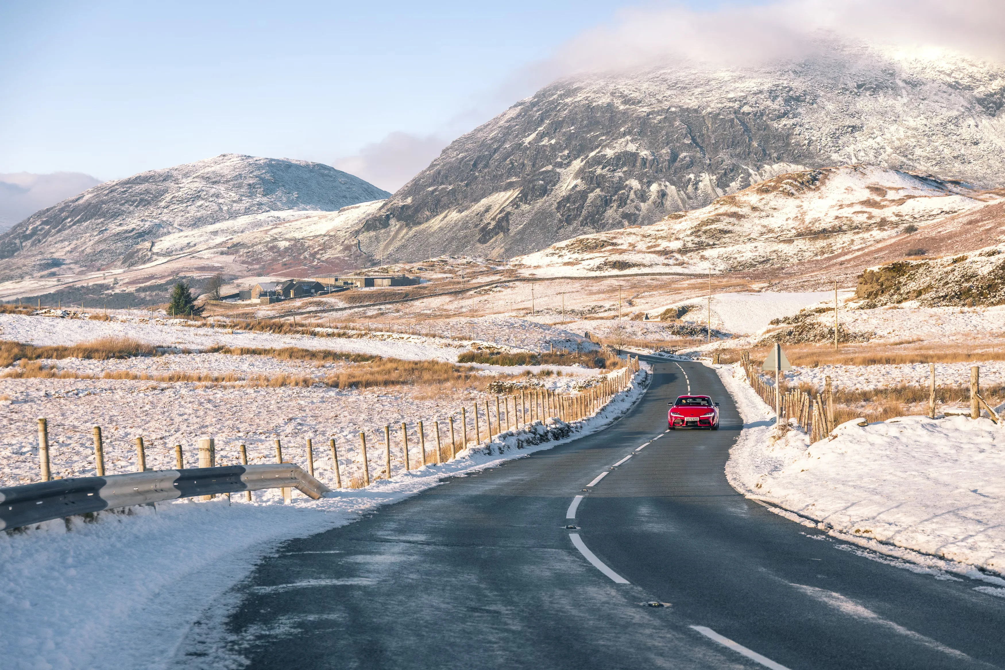 Toyota Supra manual review Rush Magazine - wide angle shot of red A90 Supra driving through Snowdonia National Park framed by snow capped mountains