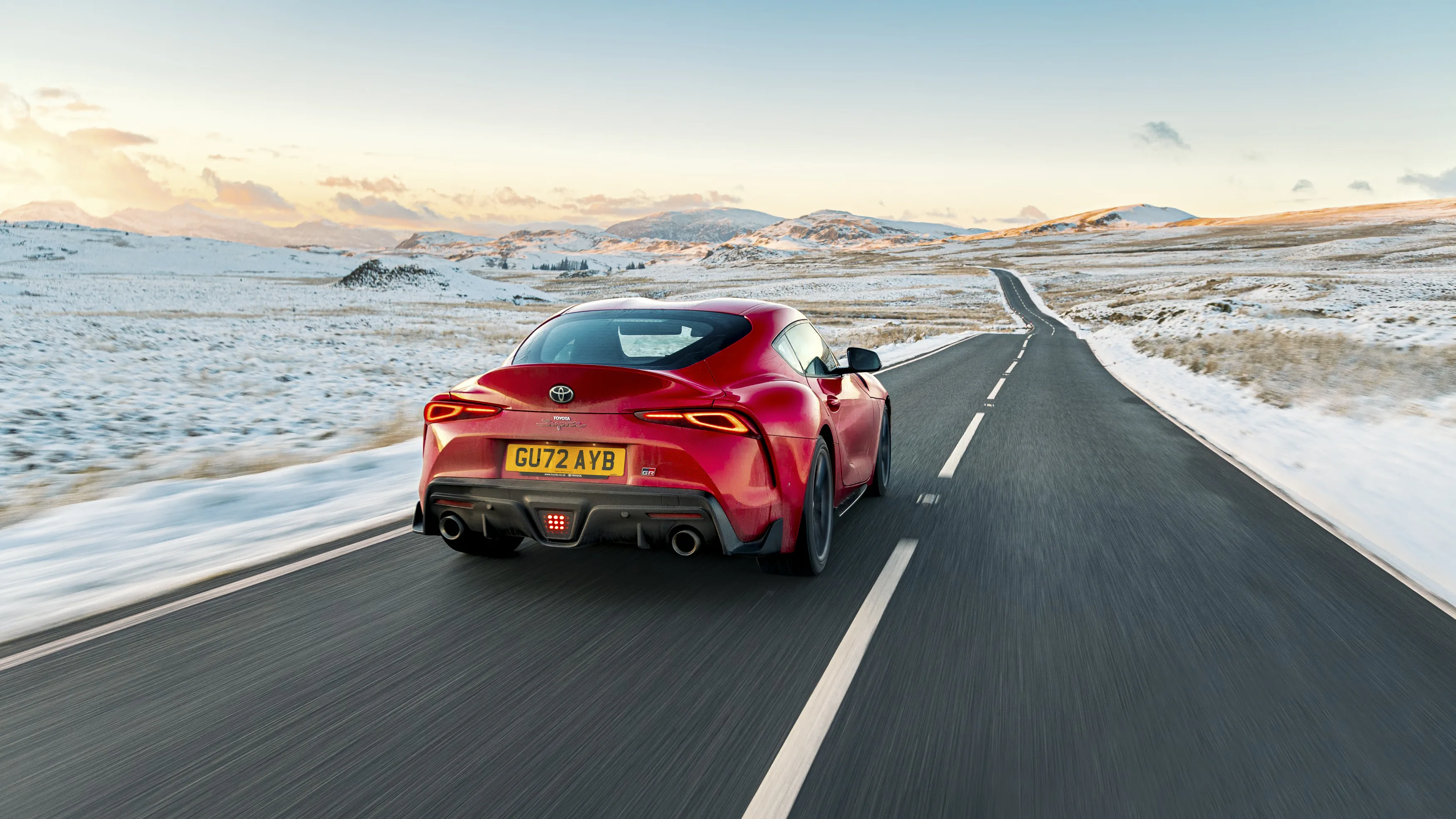 Toyota Supra manual review Rush Magazine - rear tracking shot of red A90 Supra driving through Snowdonia National Park at dusk framed by distant snow capped mountains
