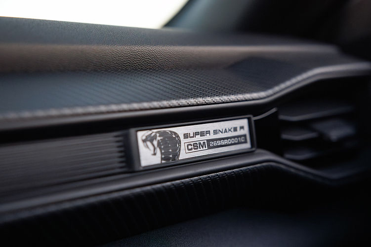Detail of the Shelby Super Snake-R’s numbered dash plaque, displaying the Cobra logo and unique CSM production number, set into a carbon-trimmed interior panel.