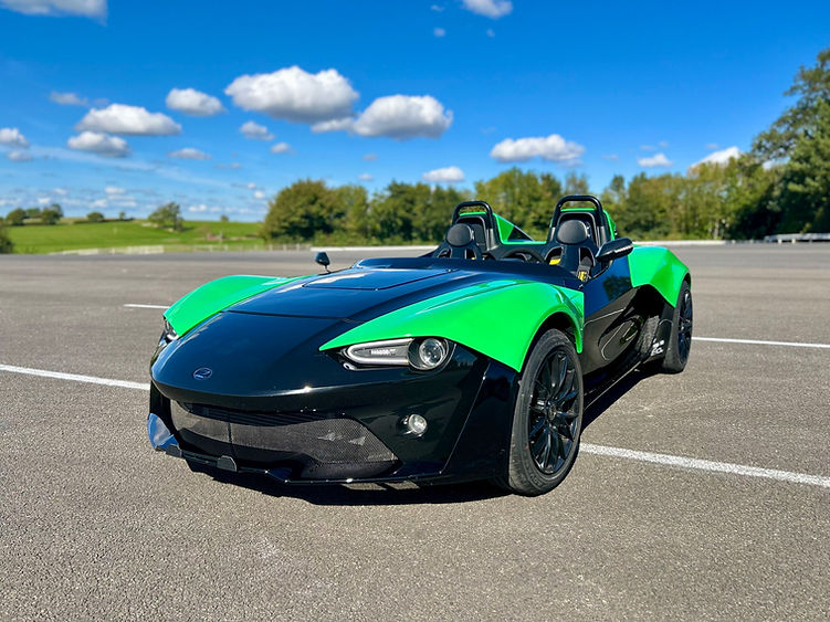 Front view of the Zenos E10 RZ under blue skies, showing its open-cockpit layout and aerodynamic design.