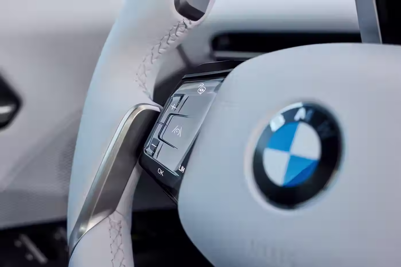 Close-up of the BMW iX3 50 xDrive's steering wheel controls with contrast stitching and BMW logo.
