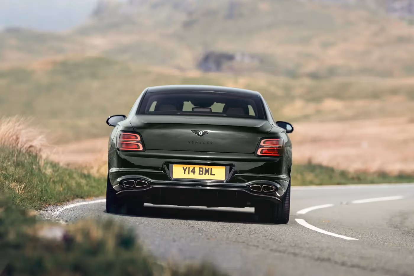 2026 Bentley Flying Spur S rear three-quarter driving shot on moorland road