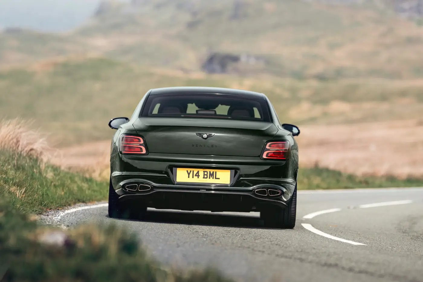 2026 Bentley Flying Spur S rear three-quarter driving shot on moorland road