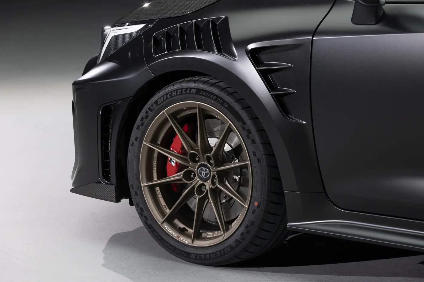 Toyota GRMN Corolla front wheel detail showing louvred wing vents, bronze wheel and red brake caliper