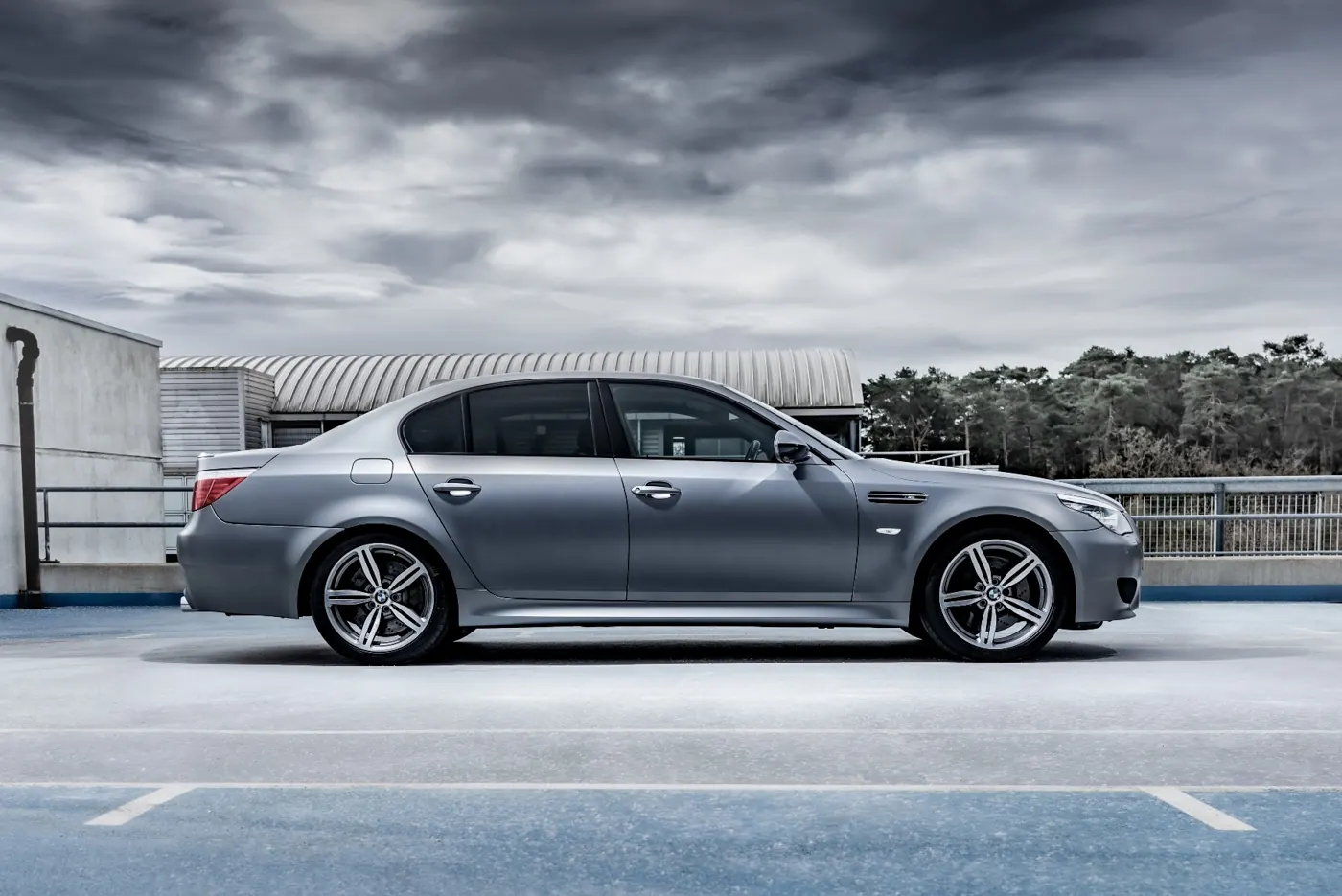Rush magazine review of silver grey metallic E60 BMW M5. Static side profile image taken at a rooftop parking garage on an overcast day