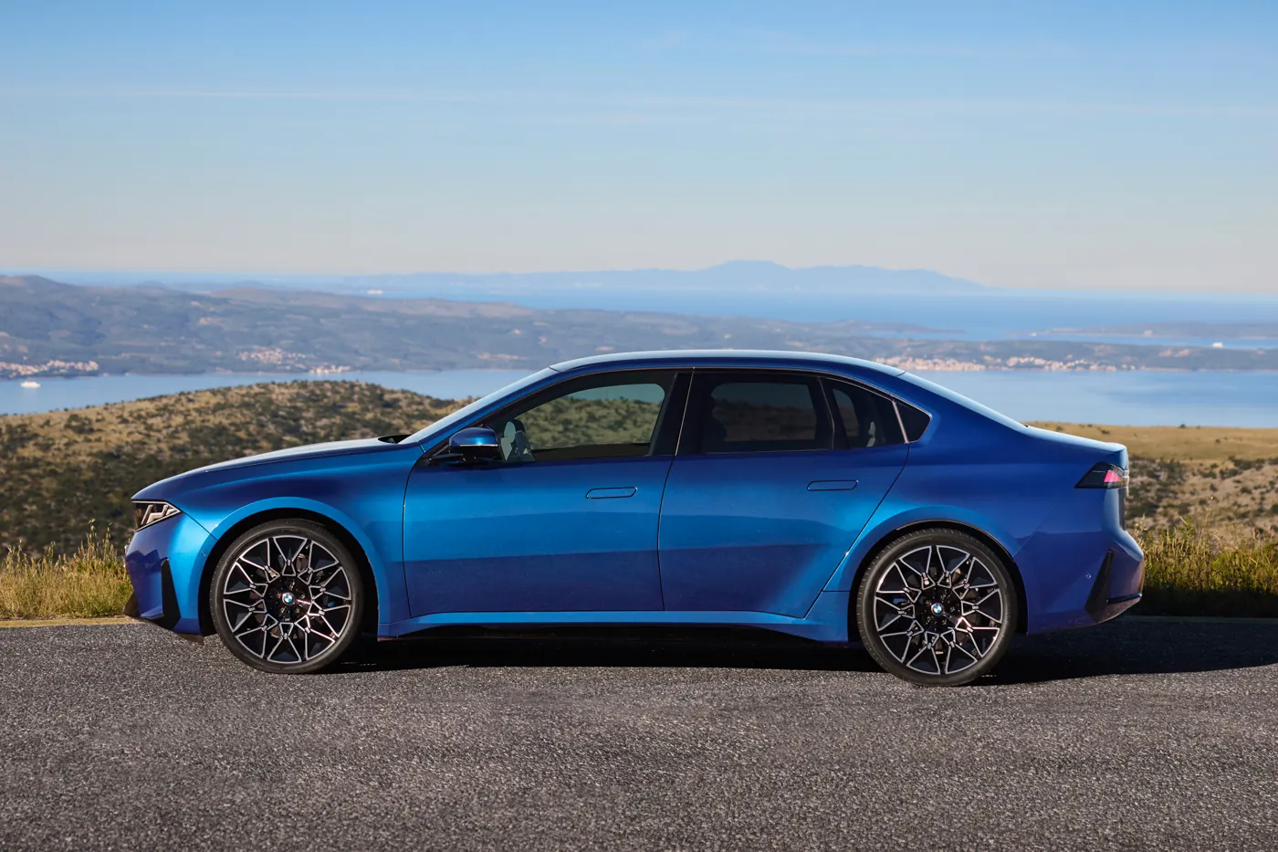 Blue BMW i3 50 xDrive electric saloon side profile on a coastal road