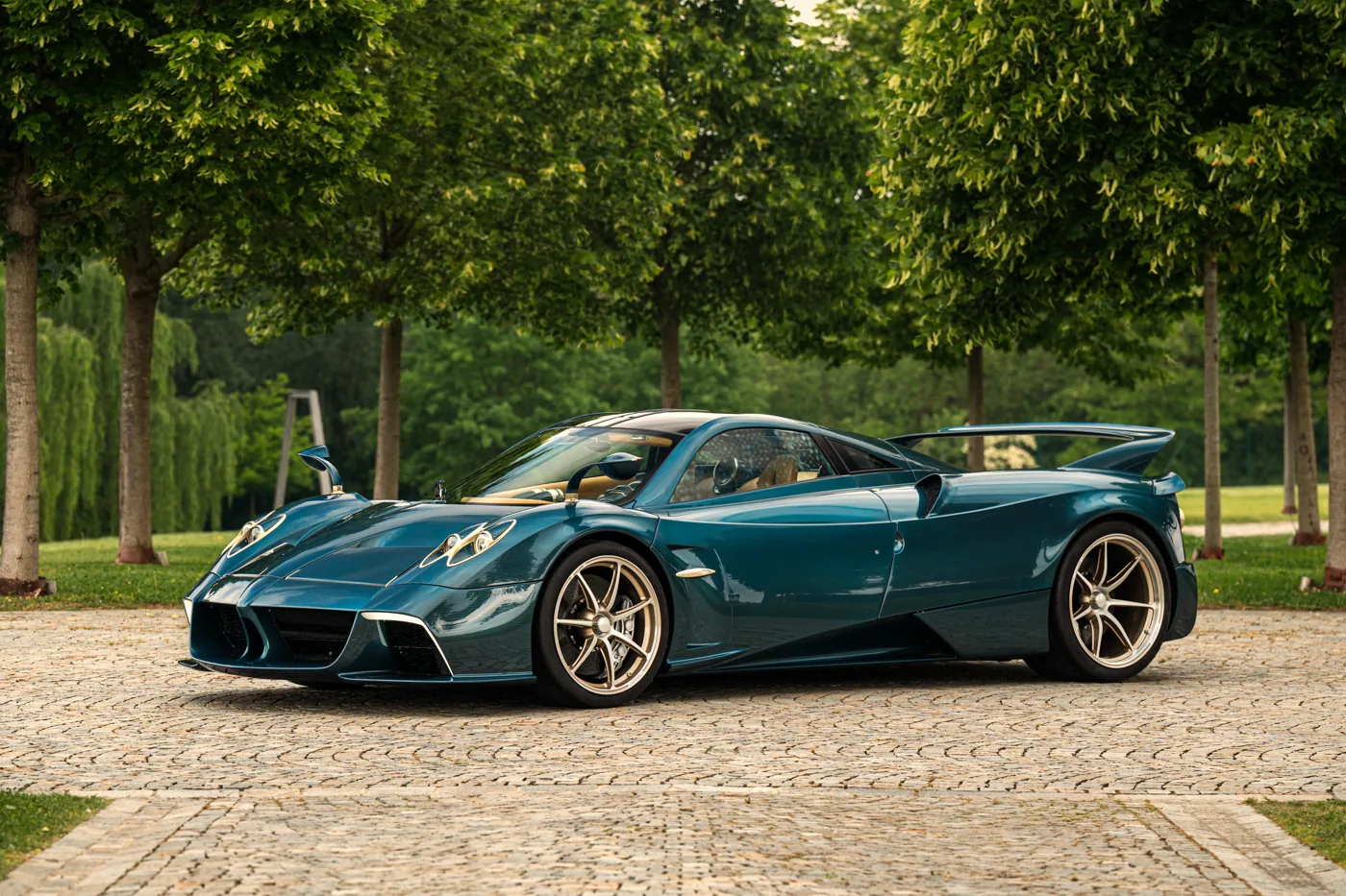 Pagani Huayra Epitome in blue-tinted carbon fibre, front three-quarter view on cobbles beneath trees