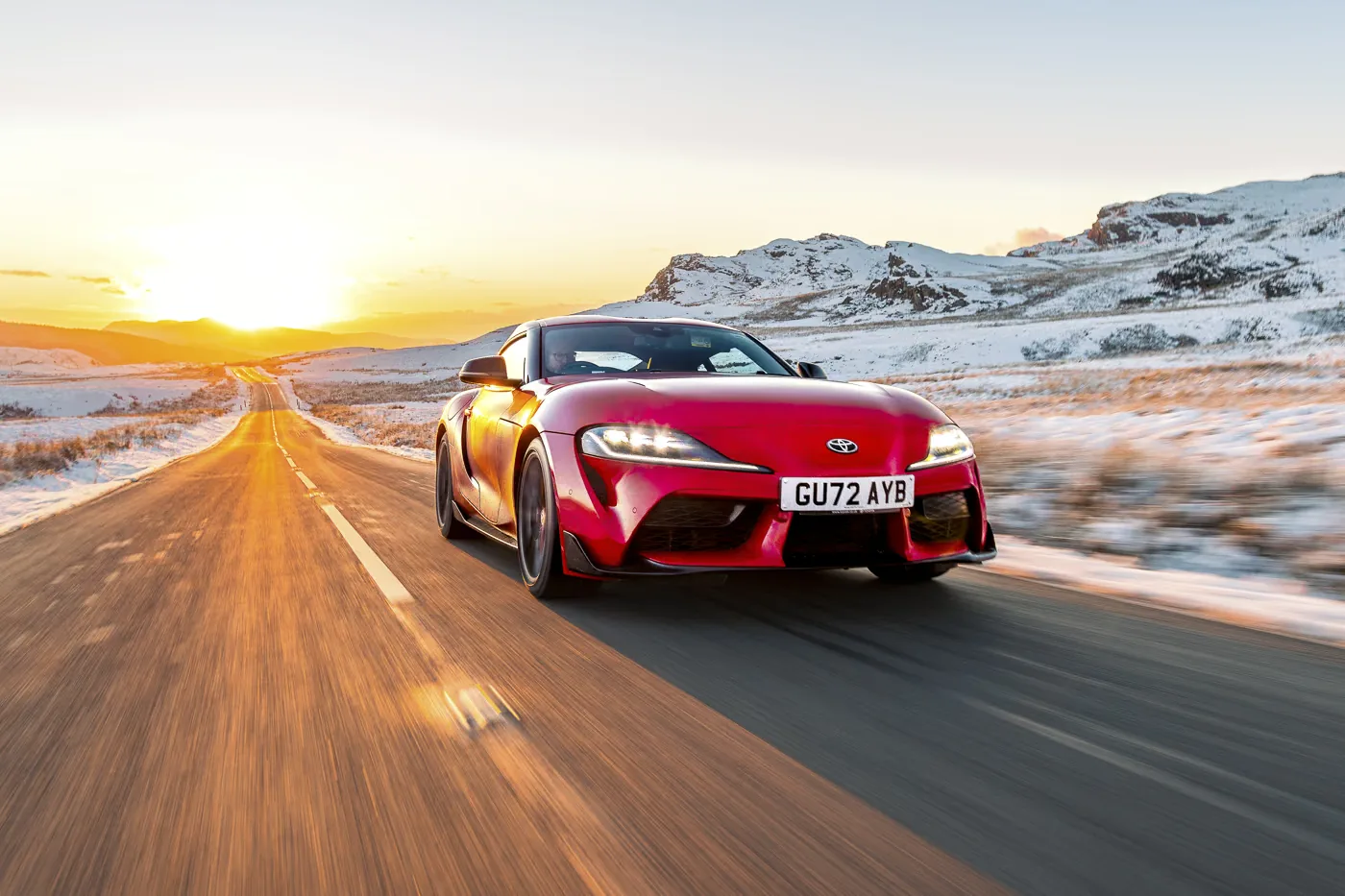 Toyota Supra manual review Rush Magazine - front three quarter tracking shot of red A90 Supra driving through Snowdonia National Park framed by snow capped mountains