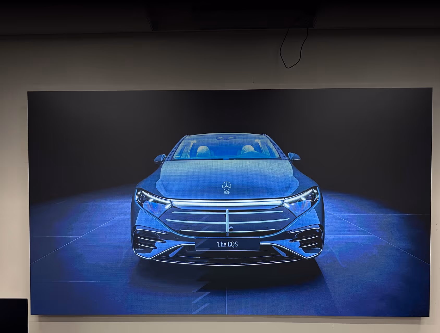Front view of a blue Mercedes-Benz EQS electric car with illuminated headlights and grille in a dark showroom.
