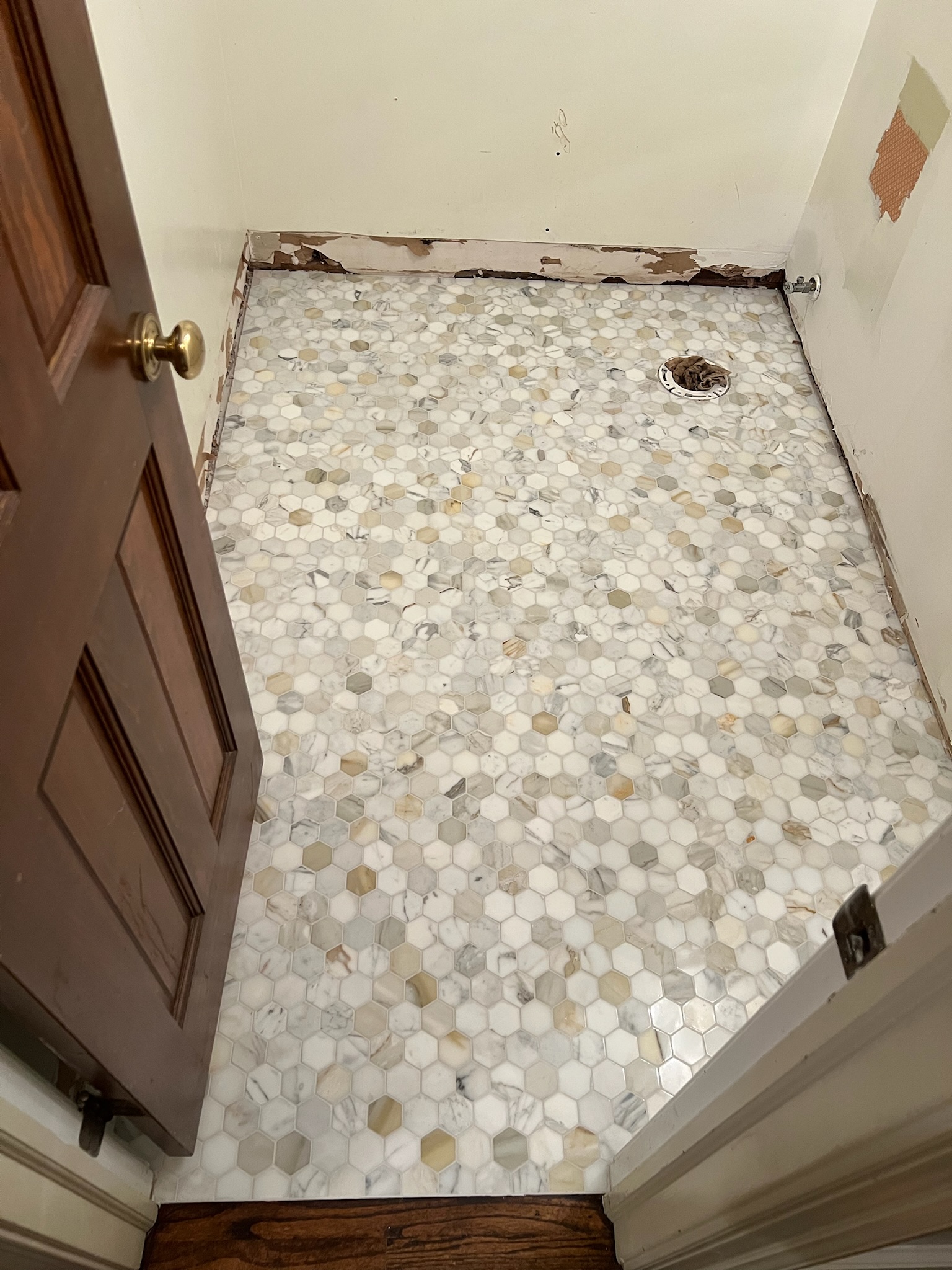 Small bathroom with newly installed hexagonal marble floor tiles and an open wooden door.