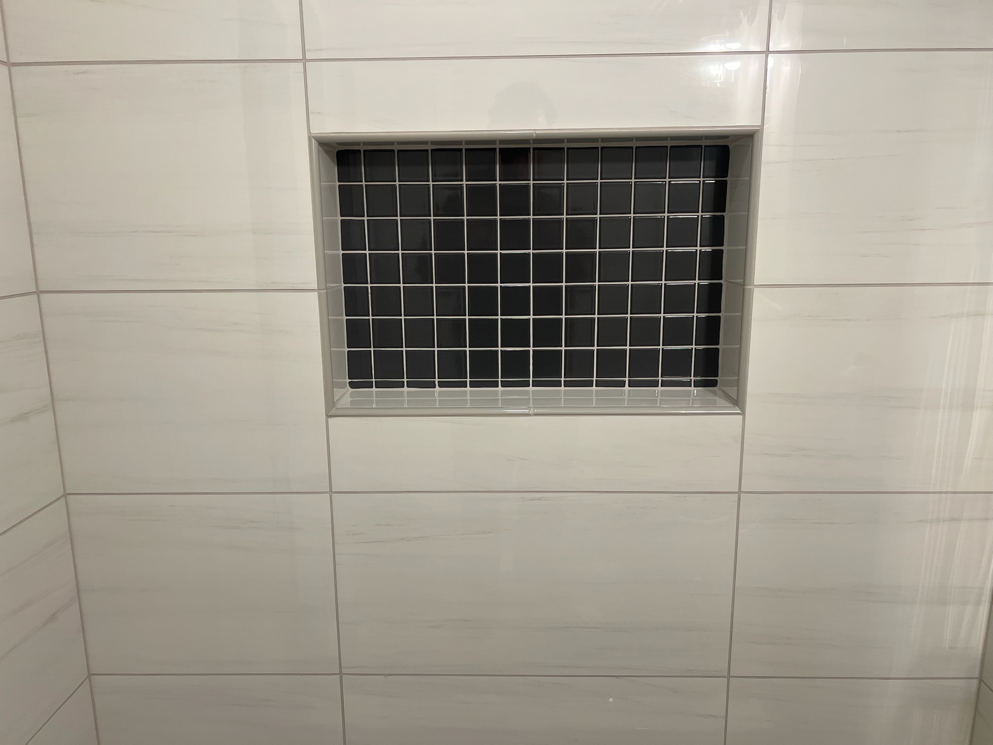 Wall niche tiled with small black square tiles surrounded by large white rectangular tiles.
