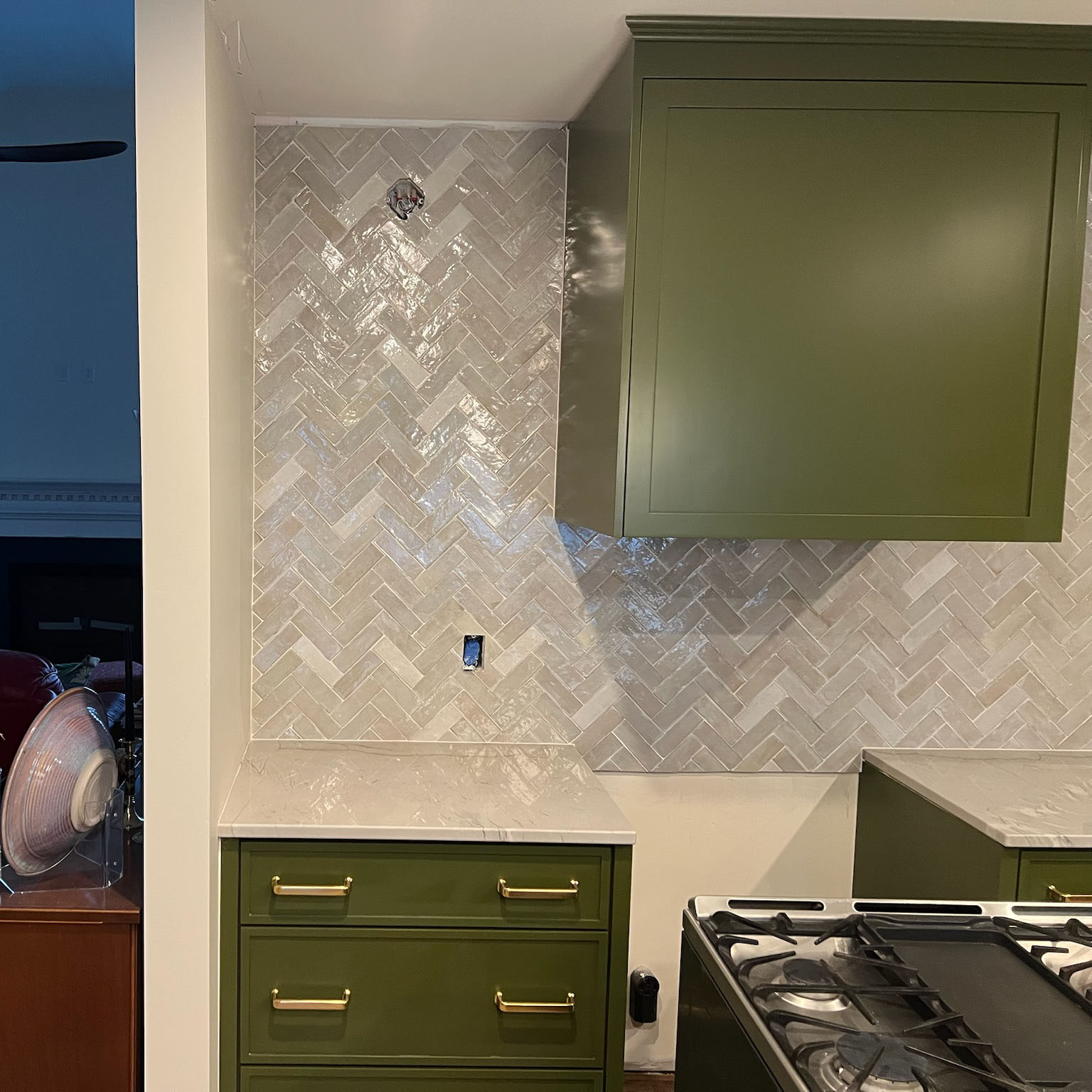 Kitchen section with green cabinets, white marble countertops, and glossy beige herringbone tile backsplash.