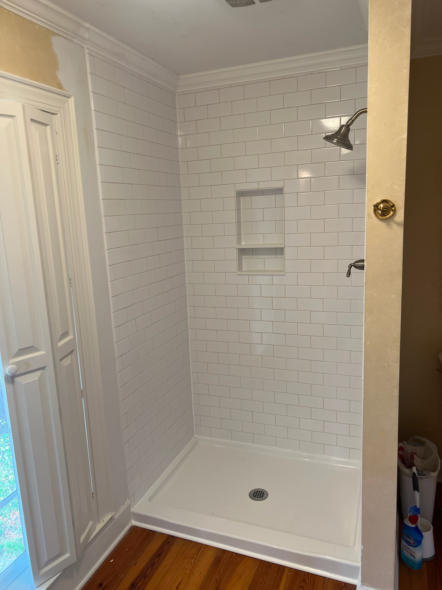 Bathroom shower with white subway tile walls, built-in shelves, silver showerhead, and white shower base on wood floor.