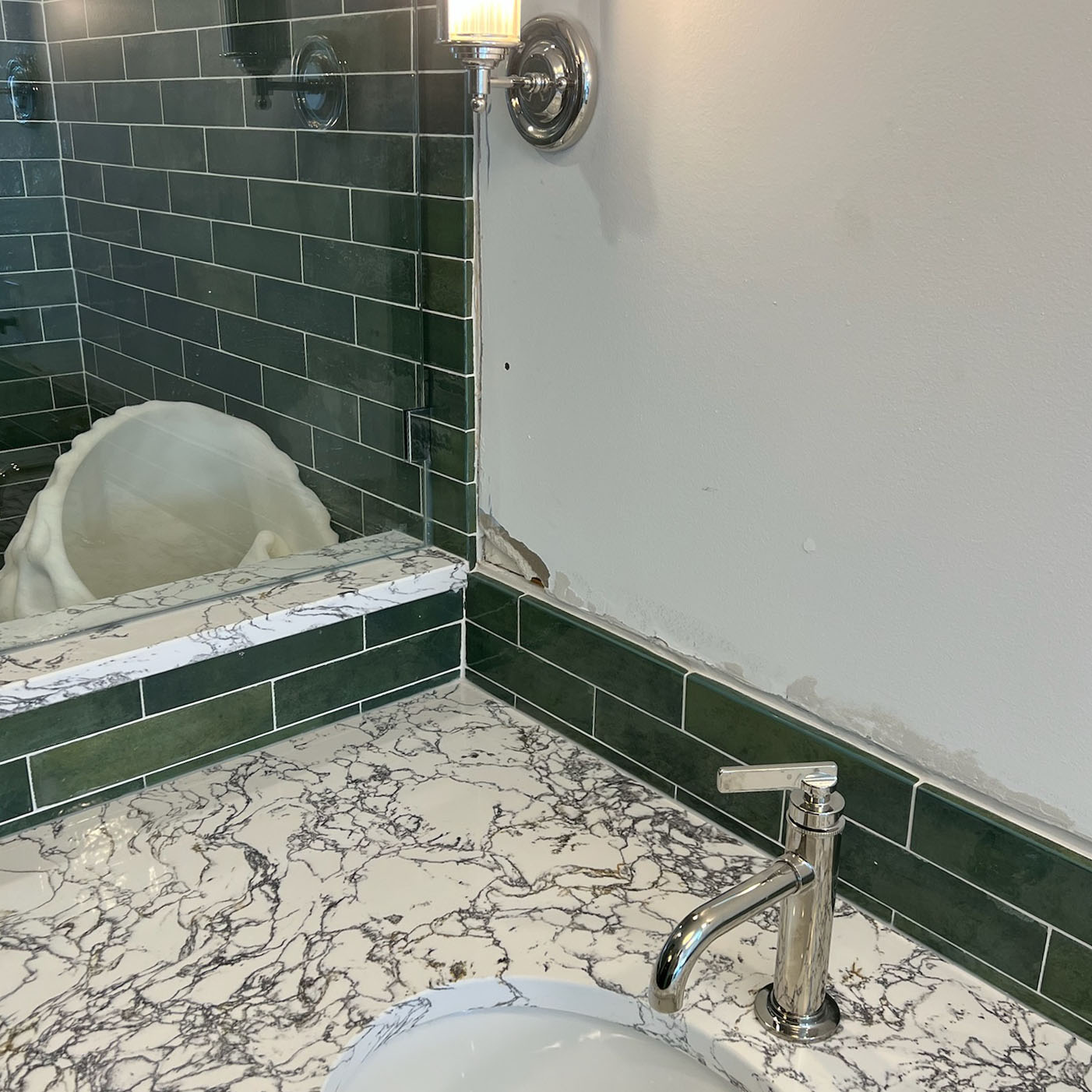 Bathroom countertop with white and gray marble pattern, a chrome faucet, and green subway tile backsplash.