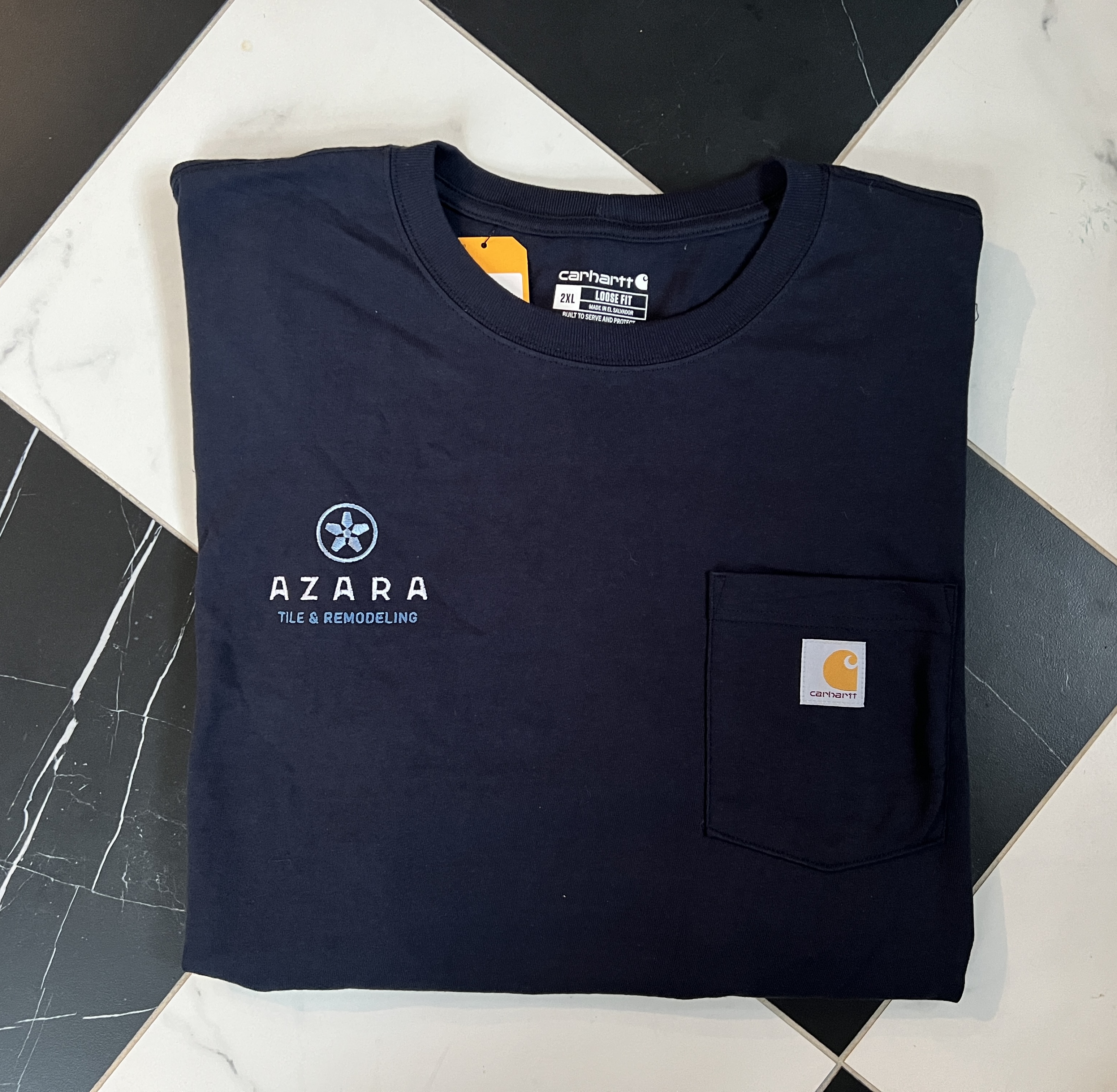 Folded navy blue Carhartt loose fit T-shirt with Azara Tile & Remodeling logo on the front left chest and a small pocket with Carhartt label.
