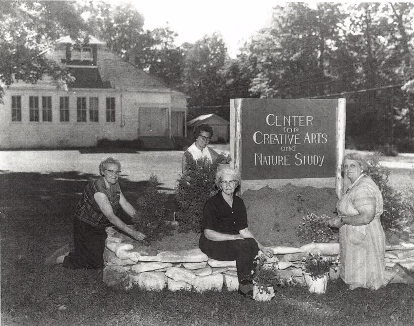 A photo of four ladies in front of the current ANC with a sign that says, "Center for Creative Arts and Nature Study"