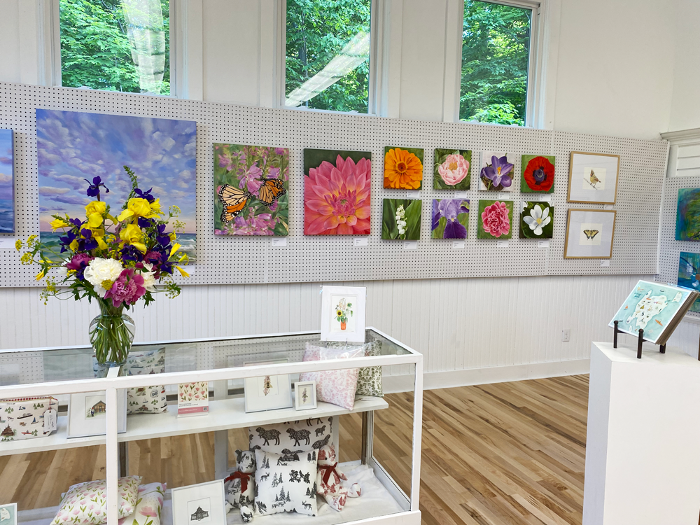 wall of paintings with flower arrangement on glass case filled with textiles and prints