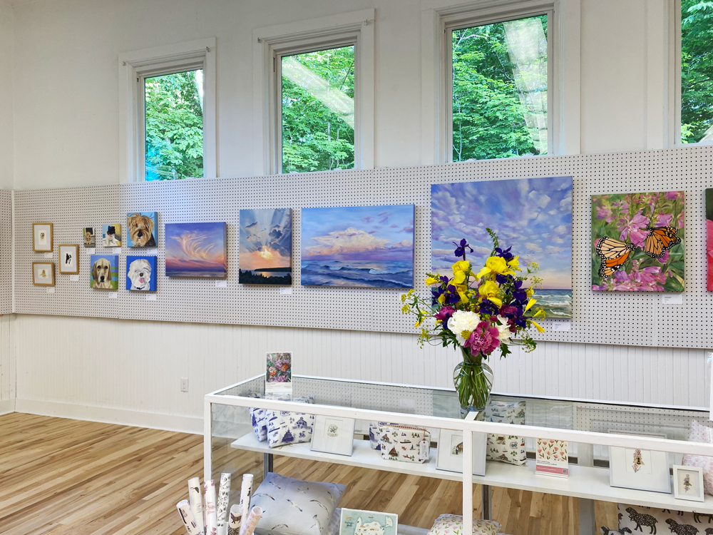 wall of paintings with flower arrangement on glass case filled with textiles and prints