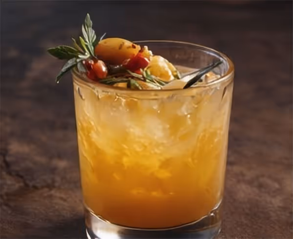 A glass of yellow liquid with a sprig of mint on top.