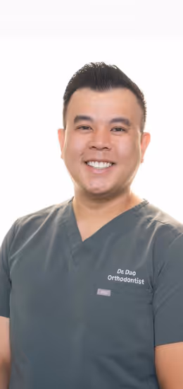 Smiling male orthodontist wearing grey scrubs with Dr. Dao Orthodontist embroidered on chest.