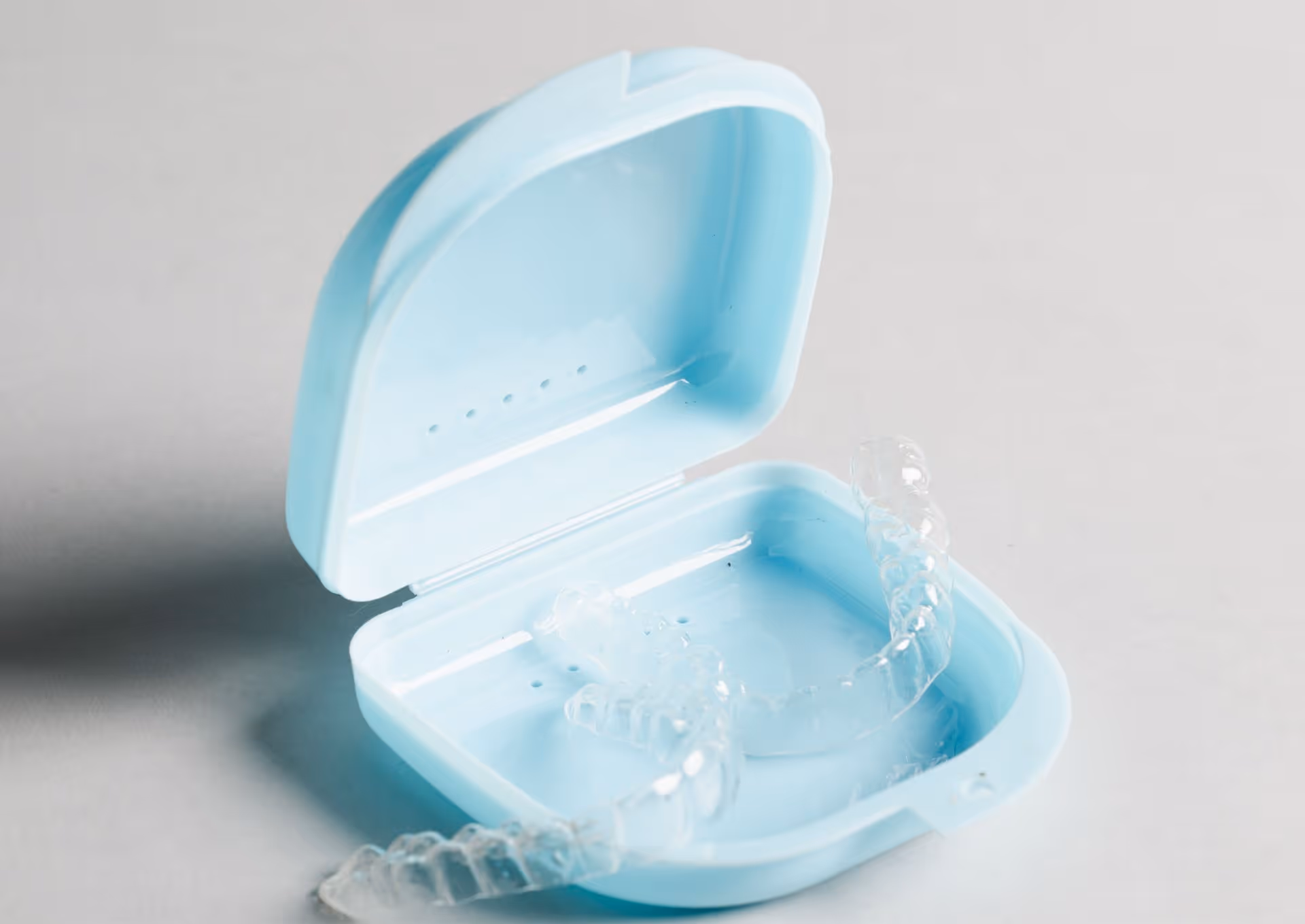 Clear dental aligners resting in an open light blue plastic carrying case on a gray surface.