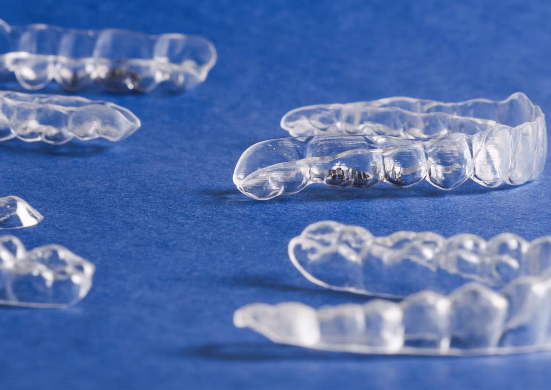 Multiple clear dental aligners placed on a blue surface.