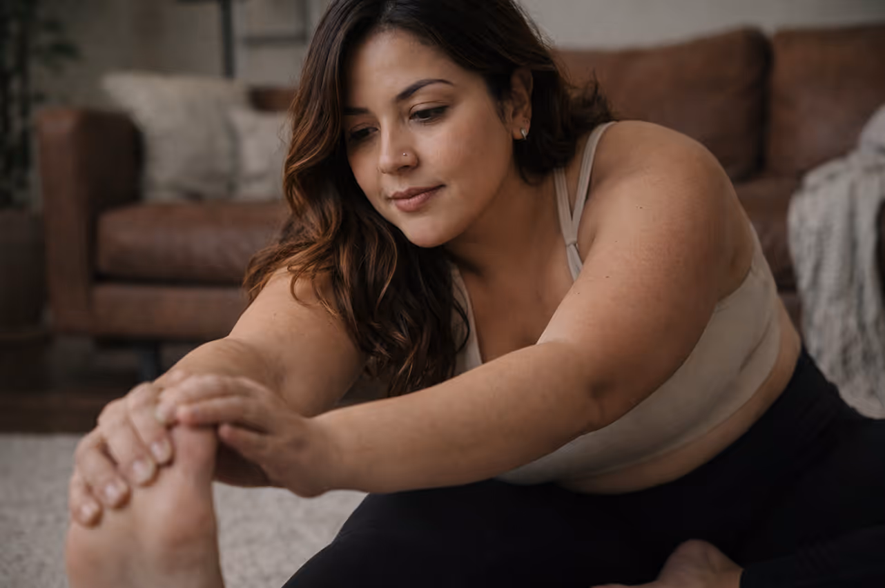 Woman stretching forward to touch her foot while sitting on the floor in a living room.