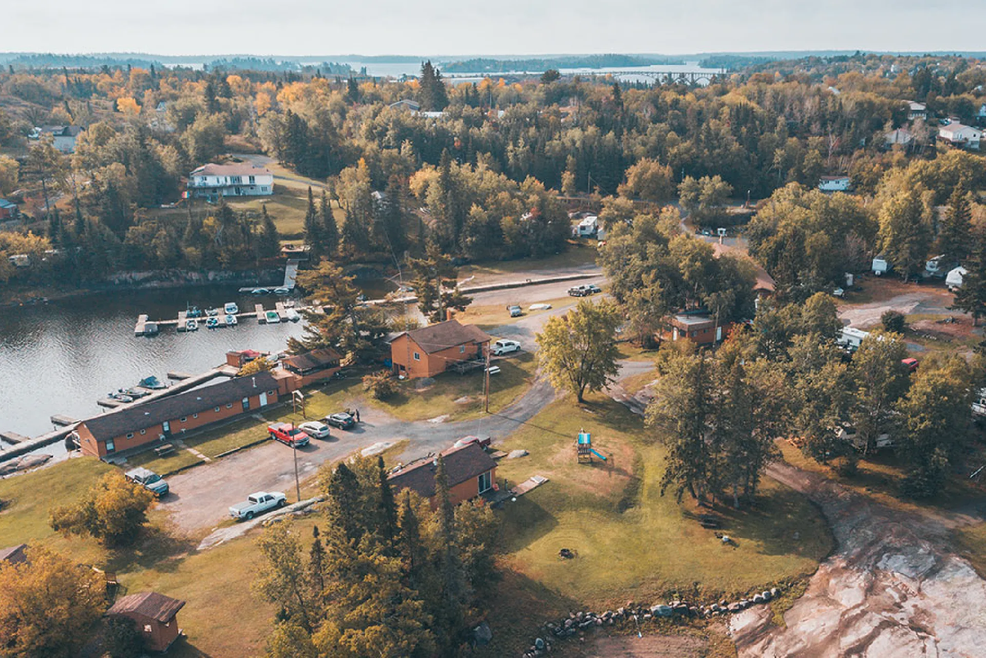 Aerial view of Perch Bay Resort grounds with cabins, parked vehicles, a playground, docks and surrounding trees.