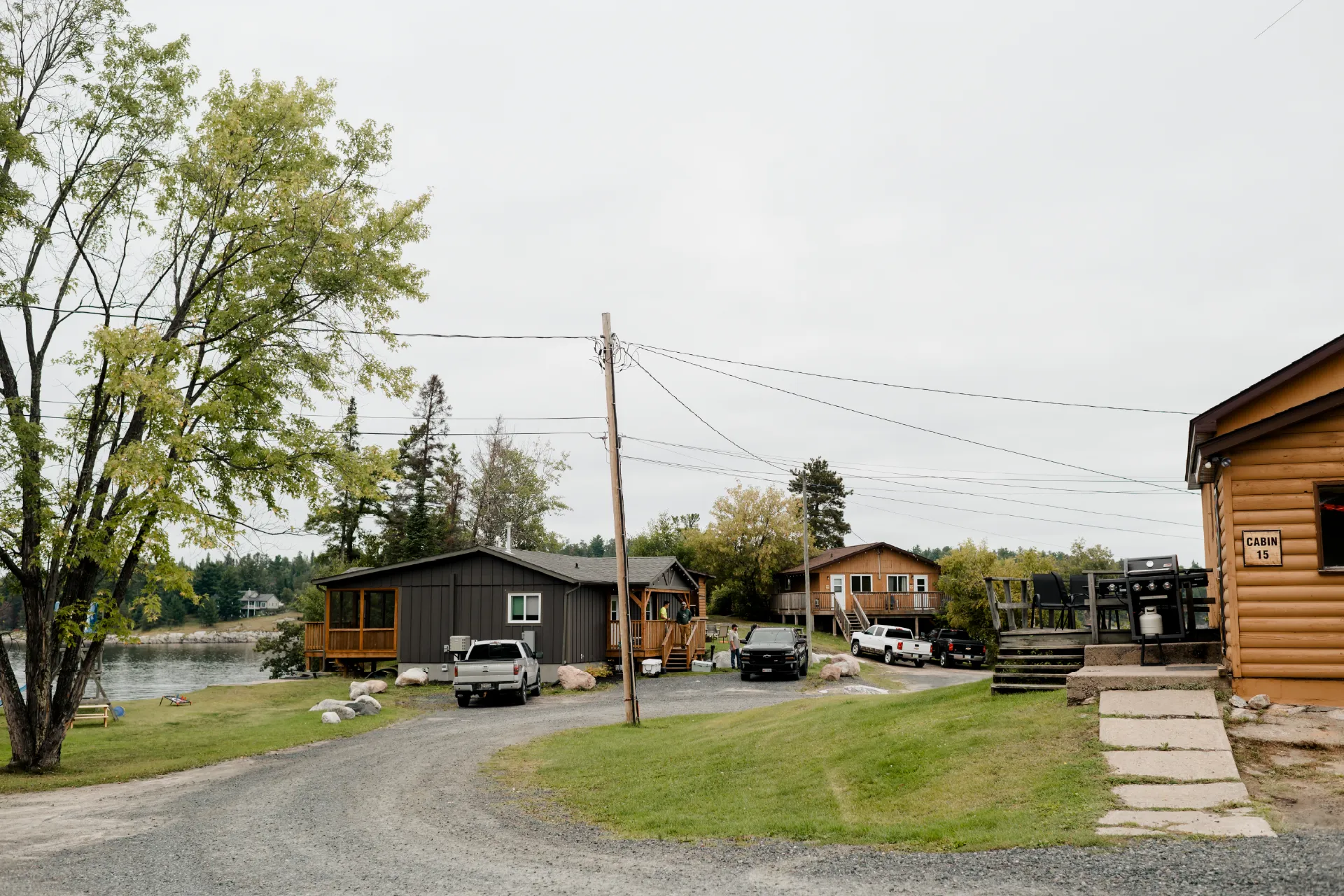 Gravel road between cabins at Perch Bay, with parked vehicles, grass and the river nearby.