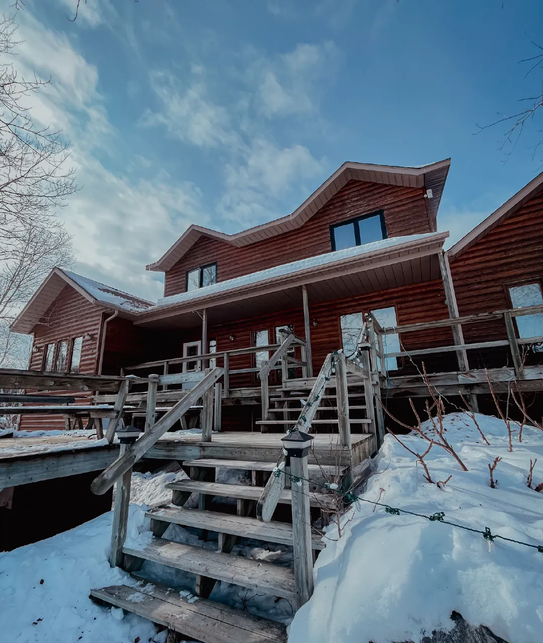 Log lodge exterior with wooden stairs and railings surrounded by snow.