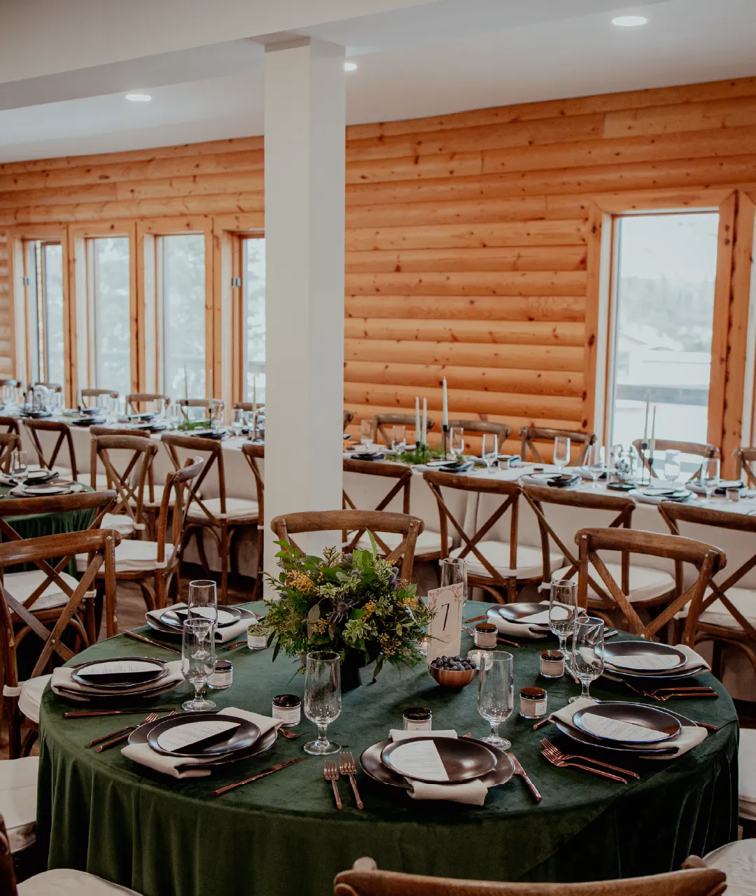 Round wedding reception table with green linens, place settings and floral centrepiece inside the lodge.