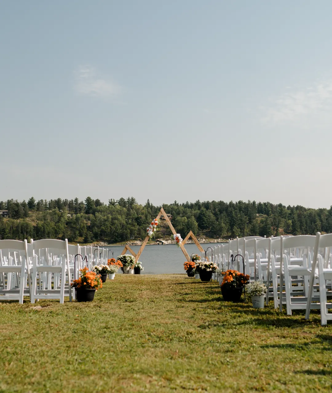 Outdoor wedding ceremony setup with white chairs, flowers and a wooden arch overlooking the river.