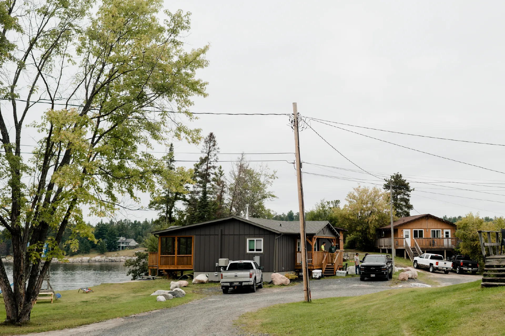 Cabins, parked vehicles and a gravel road on the resort grounds with the river in the background.
