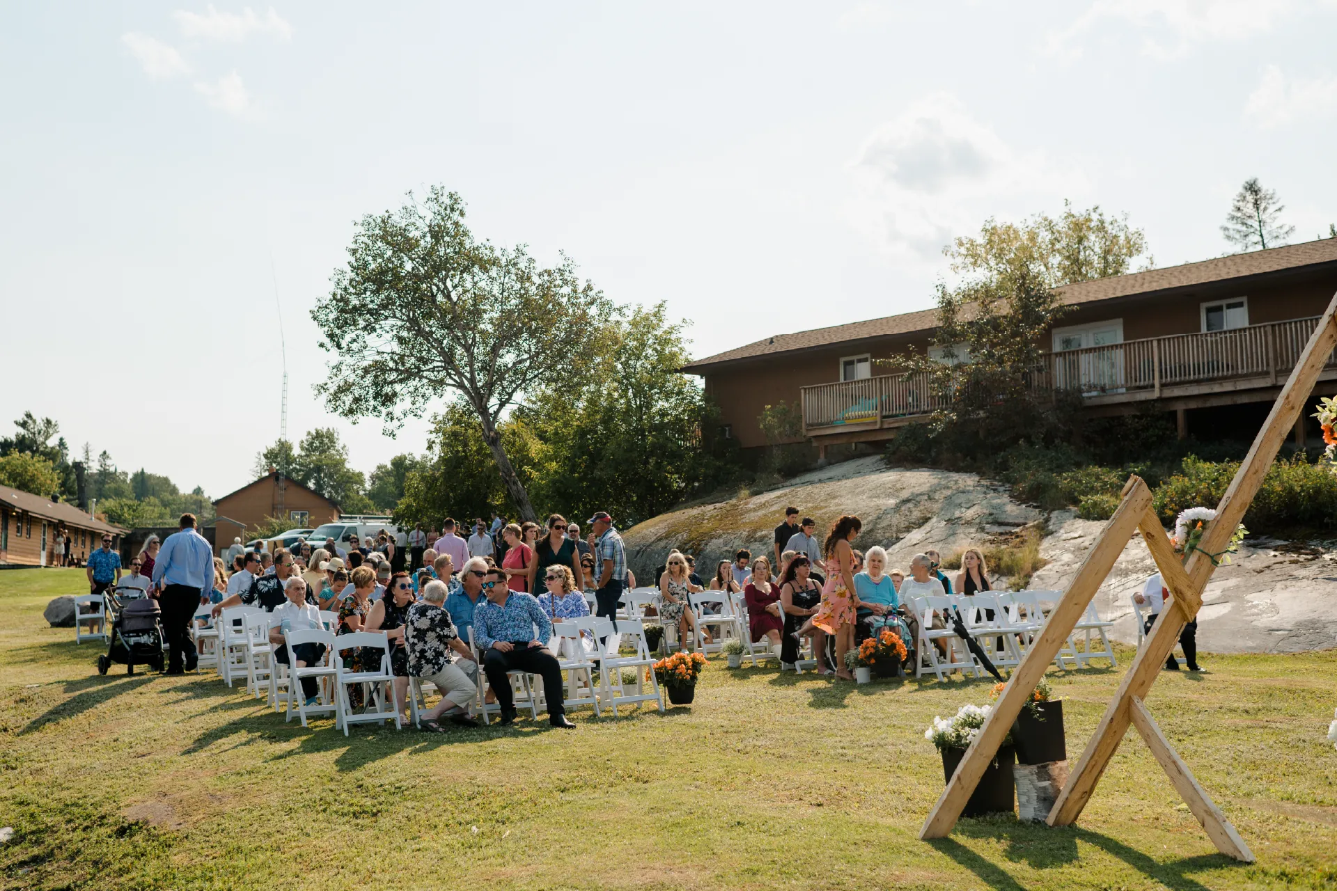 Wedding guests seated outdoors near a wooden ceremony arch, cabins and rocky resort grounds.