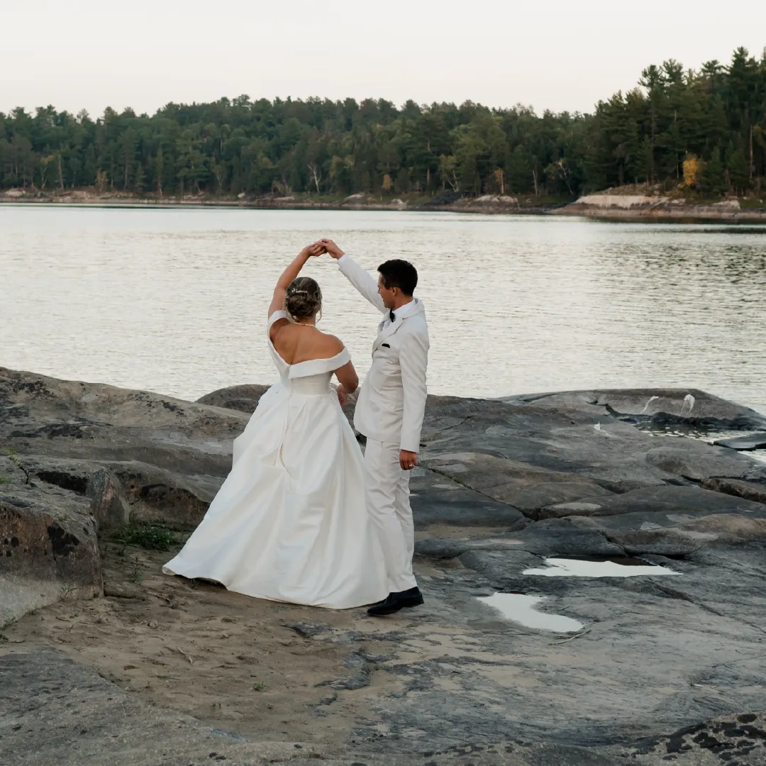 Wedding couple dancing together on a rocky shoreline beside the water.