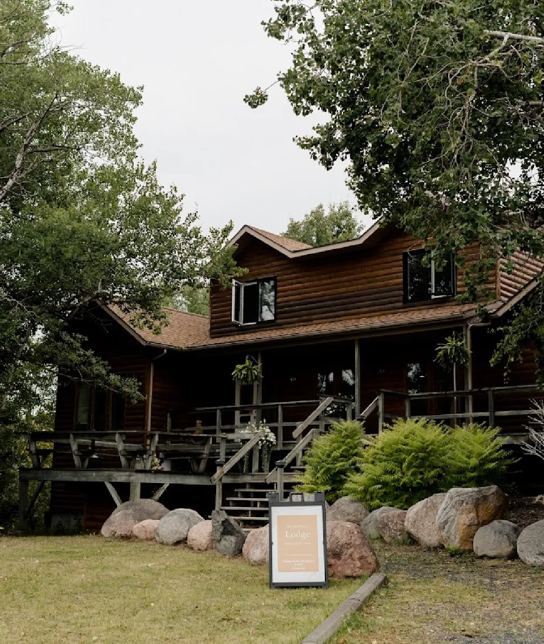 Exterior of The Lodge at Perch Bay with a wooden deck, trees, boulders and a sign on the lawn.