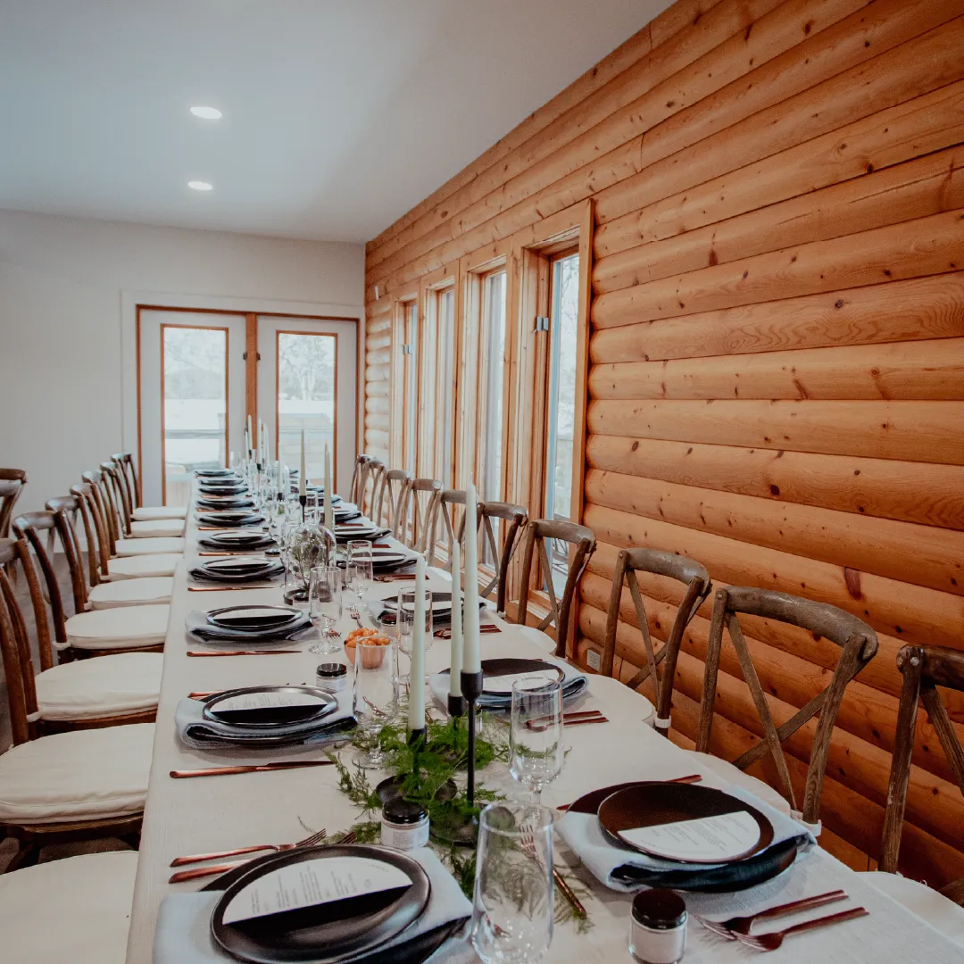 Long wedding reception table set with candles, glassware and place settings beside a wood-paneled wall.