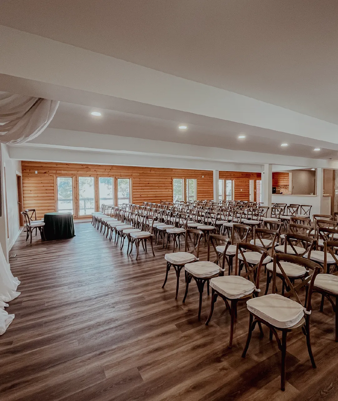 Lodge event room arranged with rows of wooden chairs facing a small ceremony table near tall windows.
