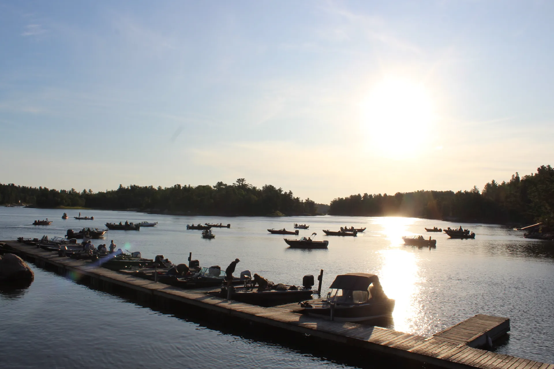Boats gathered on the water near the dock at sunset.