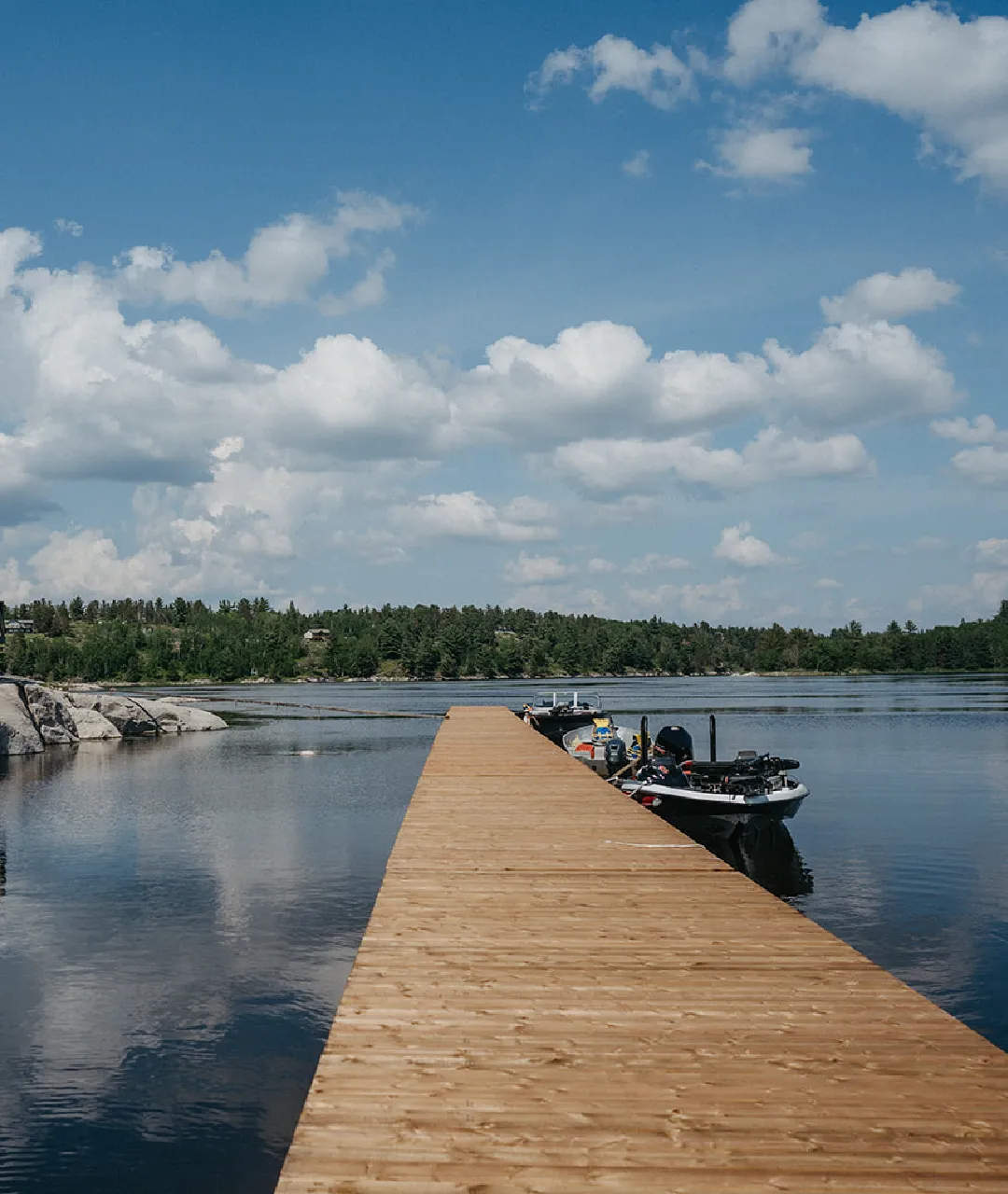 Long wooden dock with boats tied up on calm water under a blue sky.