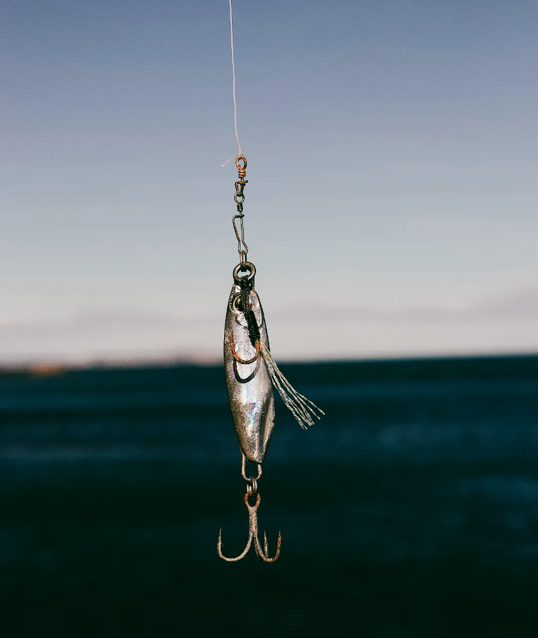 Close-up of a silver fishing lure hanging from a line with water in the background.