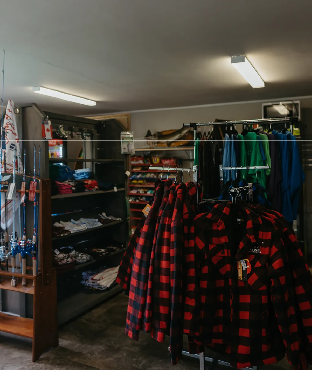 Resort store interior with plaid jackets, clothing, fishing rods and shelves of supplies.