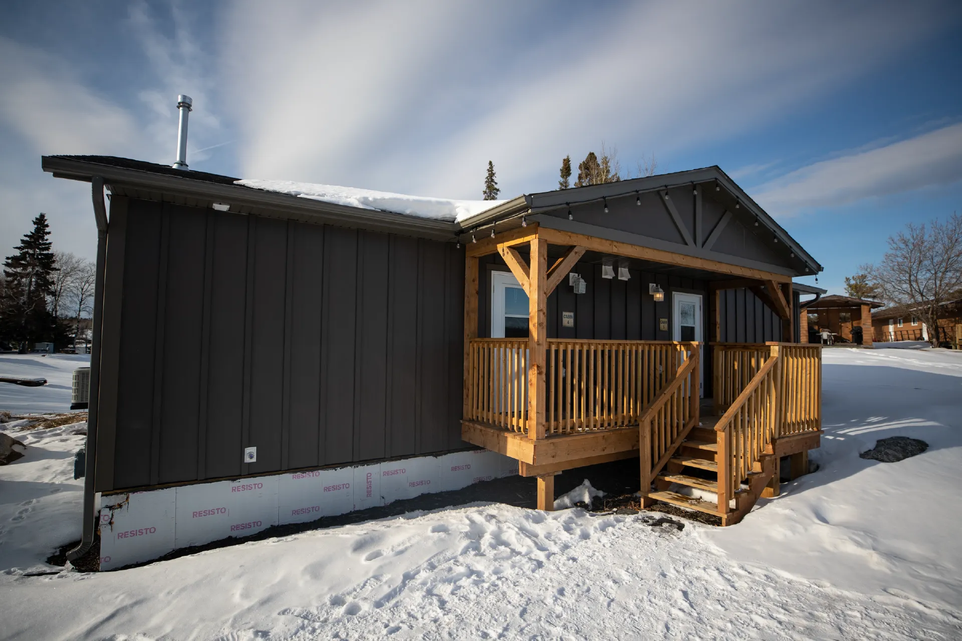 Dark cabin with a wooden front porch surrounded by snow.